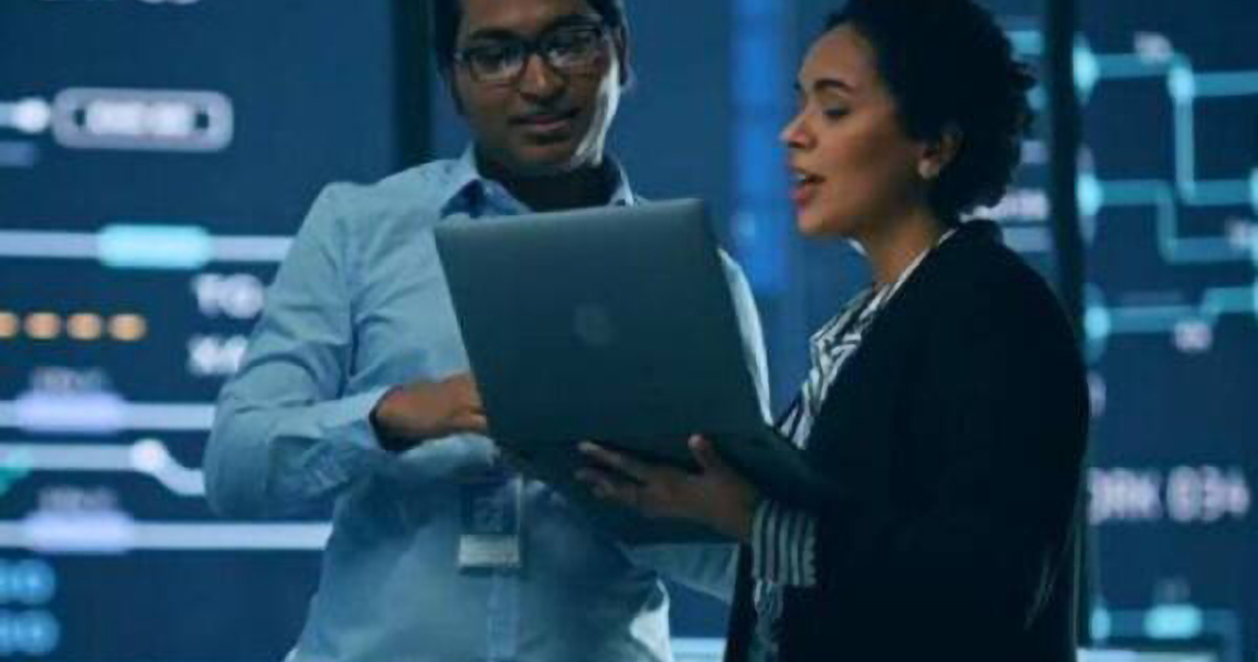 Two employees discussing while looking at a laptop in a control center