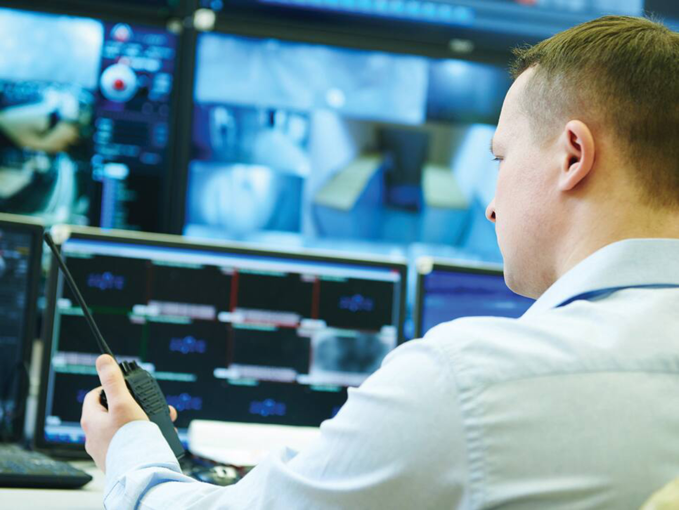 Back view of a security personnel holding a walkie talkie and monitoring the cctv footages